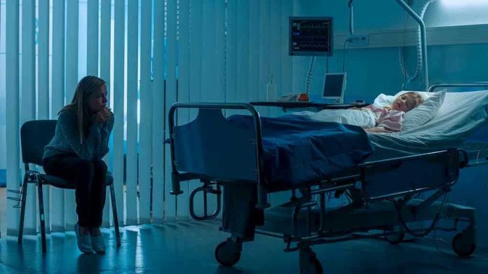 1181842819 Woman sitting beside hospital bed at night