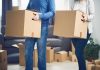 Two people carrying cardboard boxes indoors