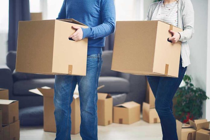 Two people carrying cardboard boxes indoors