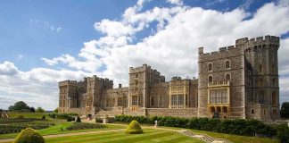 A historic castle surrounded by manicured gardens under a cloudy sky