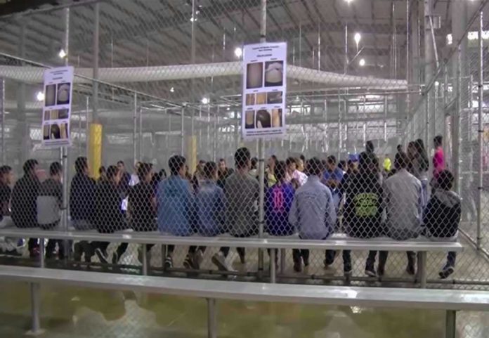 1229072206 People sitting on benches inside a fenced facility.