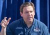 Man speaking, wearing a blue "Desantis for President" shirt.