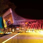 An overturned truck on the side of the road at night with emergency lights