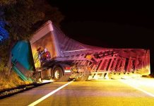 An overturned truck on the side of the road at night with emergency lights