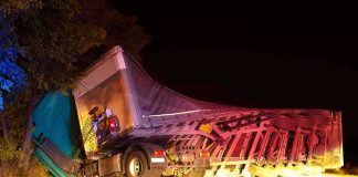 An overturned truck on the side of the road at night with emergency lights