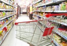 A shopping cart in a grocery store aisle filled with colorful products