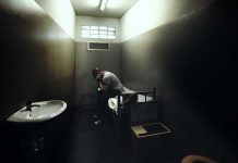 A person sitting in a dimly lit prison cell, appearing contemplative and distressed