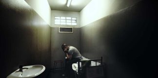 A person sitting in a dimly lit prison cell, appearing contemplative and distressed