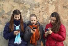 Three teenagers using smartphones while standing against a textured wall