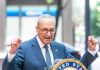 Dems  FREEZES Troop Paychecks – Cash Their Own! Man in suit and glasses speaks passionately at podium.
