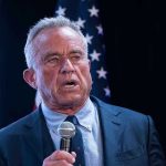 RFK Jr. Drops Jaws – RIDICULOUS Rant Man holding microphone, speaking with American flag behind.