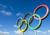 USA Olympians SUING Foundation – They’ve Had It! Olympic rings sculpture against blue sky.