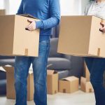 MASS EXIT: Residents FLEEING State! Two people carrying cardboard boxes indoors.