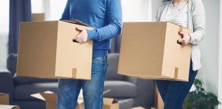 Two people carrying cardboard boxes indoors.