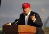 Trump APPROVES Operation – 17 Strikes, 70 DEAD Person speaking at a podium wearing a red hat.