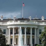 White House SLAMS Writer – Explosive Guard Shooting Debate White House with American flag and fountain, stormy sky.