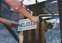 Hand placing closed sign on glass door