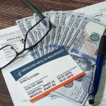 Severe Medicaid FRAUD – Dead People Paid Billions! Medicare card glasses pen money on wooden table