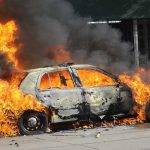 A car engulfed in flames with thick smoke billowing into the air