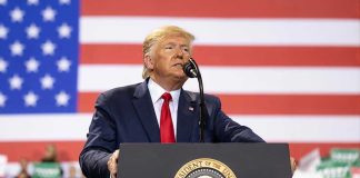 Trump’s Arch to Rival Paris Landmark – Date Set! Man speaks at podium with U.S. flag background.