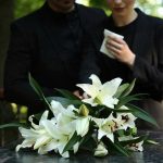 Mourners in black holding white flowers at funeral.