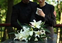 Mourners in black holding white flowers at funeral.