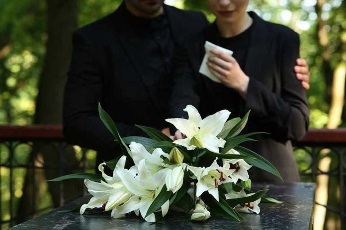 Mourners in black holding white flowers at funeral.