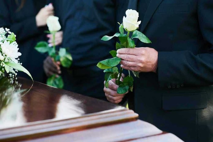 2360876145 Mourners holding white roses by a casket.
