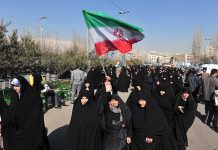 Group of women in black attire marching with an Iranian flag