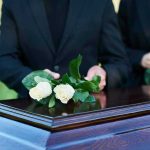 People placing white roses on a casket.