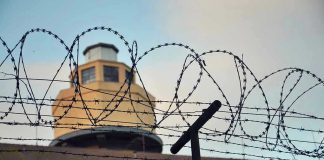 Trump REVIVES Infamous Prison – Sparks Fury! Barbed wire in front of a prison tower.