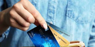 Hand holding credit cards over a brown purse.