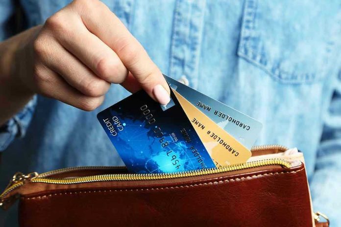 Hand holding credit cards over a brown purse.