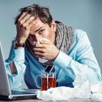 Virus Outbreak on Cruise Ship – Are You at Risk? Man with tissue feeling unwell at laptop desk