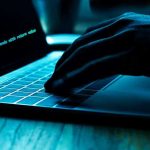 321 Foreign Workers Arrested in Shocking Cybercrime Bust Hand typing on laptop with code on screen.