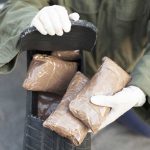 Person handling packages wearing gloves and green jacket.