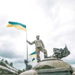 Moscow’s Chilling Ultimatum: Evacuate Kyiv NOW Soldier on tank holding Ukrainian flag.