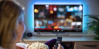 Person sitting on a couch watching a movie on a TV with popcorn in hand
