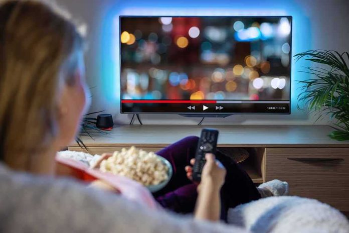 shutterstock_1966720738 Person sitting on a couch watching a movie on a TV with popcorn in hand