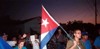Cuba’s Crisis Deepens—CIA Steps In A group of people participating in a protest march holding a Cuban flag