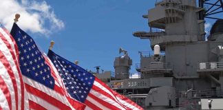 Cuba Tensions Rise as Massive Carrier Arrives American flags in front of a naval ship under a blue sky