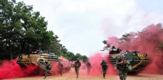 Soldiers running from armored vehicles with red smoke.