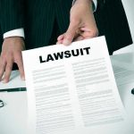 Person holding a document titled LAWSUIT in office.