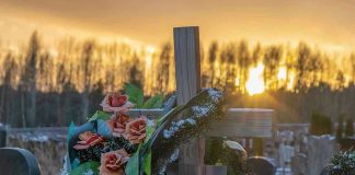 Outrage Spread Quickly After This Photo Appeared—Verification Never Did. Cross with flowers at cemetery during sunset.