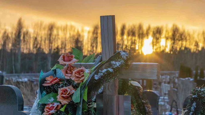 2132449505 Cross with flowers at cemetery during sunset.