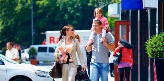 A family walking on a sidewalk in an urban area, with a child on the fathers shoulders