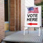 Vote Here sign with arrow and American flag.