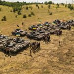 Rows of military tanks with soldiers assembled on a dry field