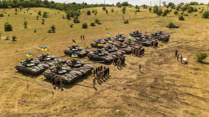 shutterstock_1789981853 Rows of military tanks with soldiers assembled on a dry field