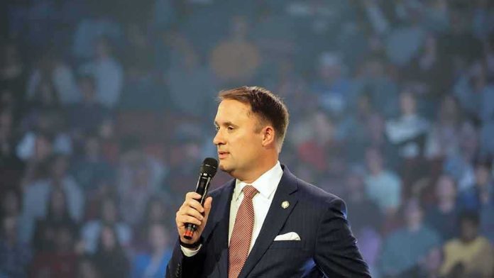 man in a suit speaking into a microphone on stage